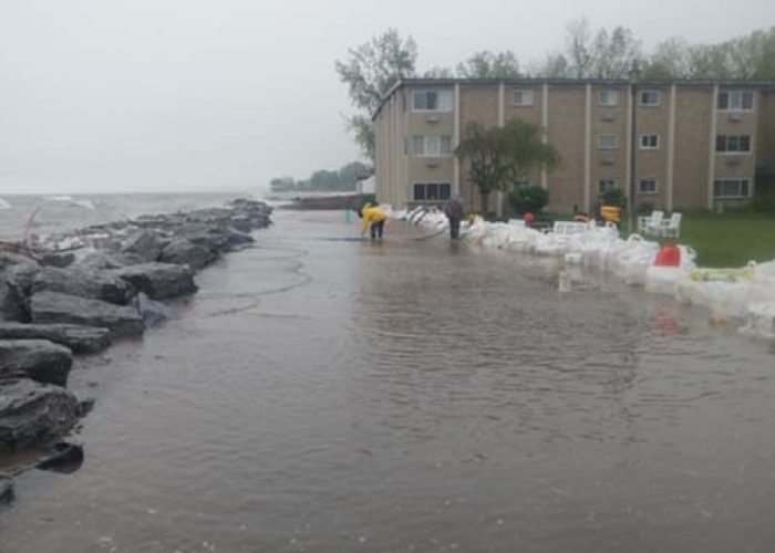 Sandbags protecting apartment building from floodwaters by a rocky shoreline.