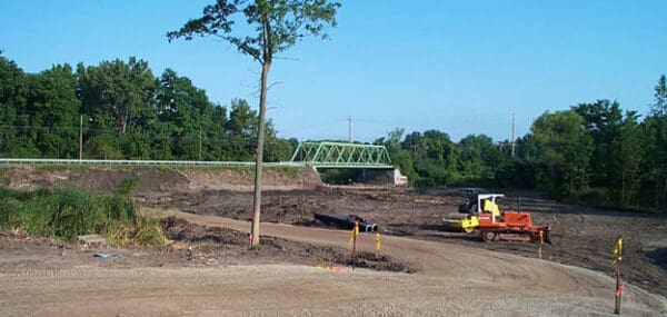 Construction site with bulldozer near a green bridge, surrounded by trees. Ideal for landscape development projects.