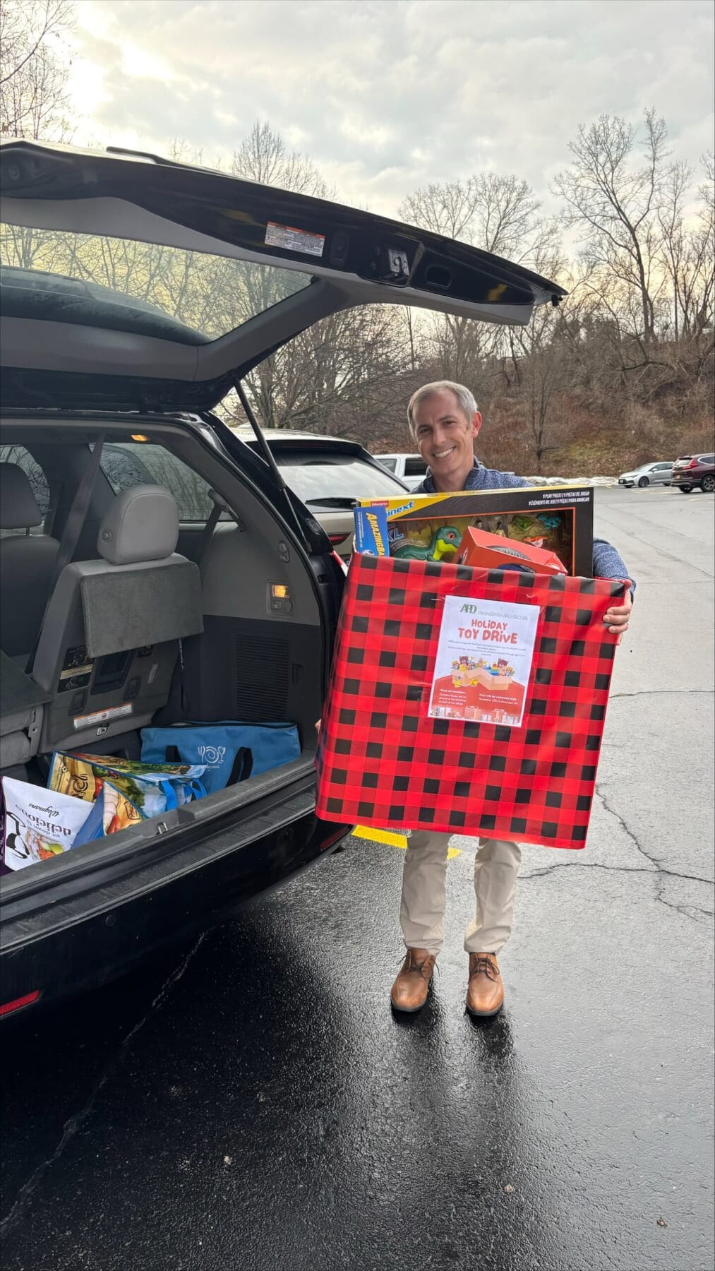 Person loading holiday toy donations into car at charity event.