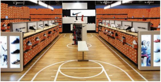 Shoe store aisle showcasing branded footwear on display shelves with vibrant orange boxes, emphasizing sports gear variety.