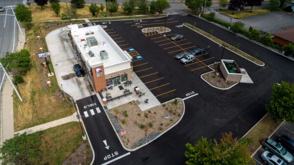 Aerial view of Taco Bell with empty parking lot on a clear day, highlighting drive-thru access and outdoor seating.