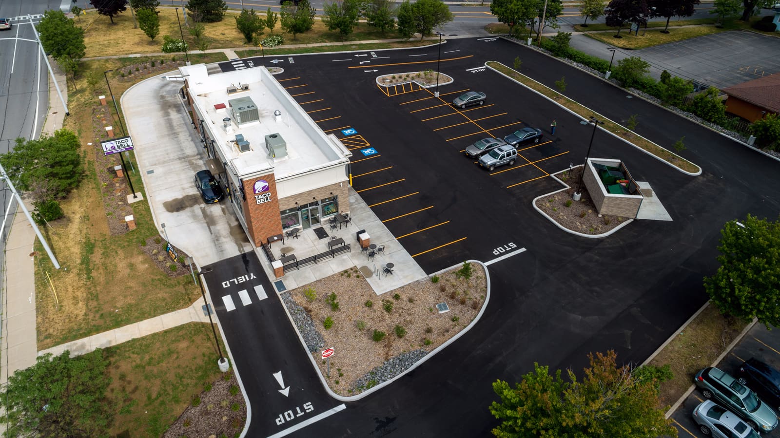 Aerial view of Taco Bell with empty parking lot on a clear day, highlighting drive-thru access and outdoor seating.